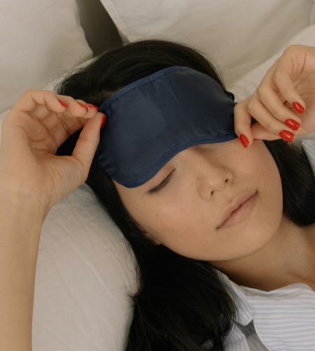 Woman gently waking up in bed, removing sleep mask with soft morning light.